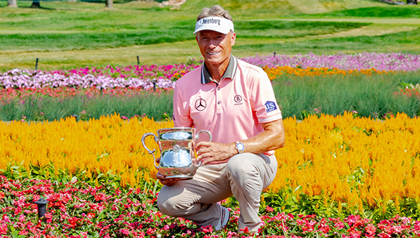Bernhard Langer holding his 2023 U.S. Senior Open championship trophy in the flowers surrounding hole 16. 
