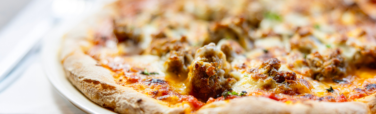 Close-up of a wood fired pizza with melted cheese, tomato sauce, and sausage toppings.
