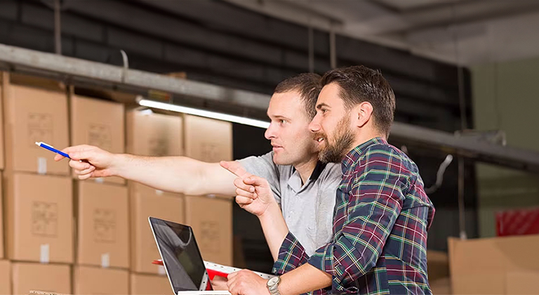 Two men with laptop pointing at something in warehouse