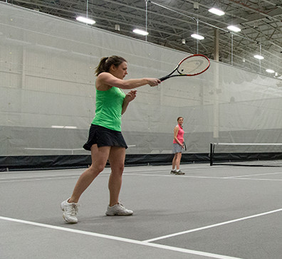 Player serving a tennis ball on a court in the fieldhouse at SentryWorld