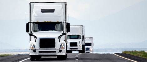 White semi trailer trucks driving down road in a line.