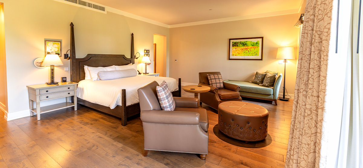 carousel-suite-golf-view-luxury-junior-2-1200x556 Room with king sized bed and seating area.