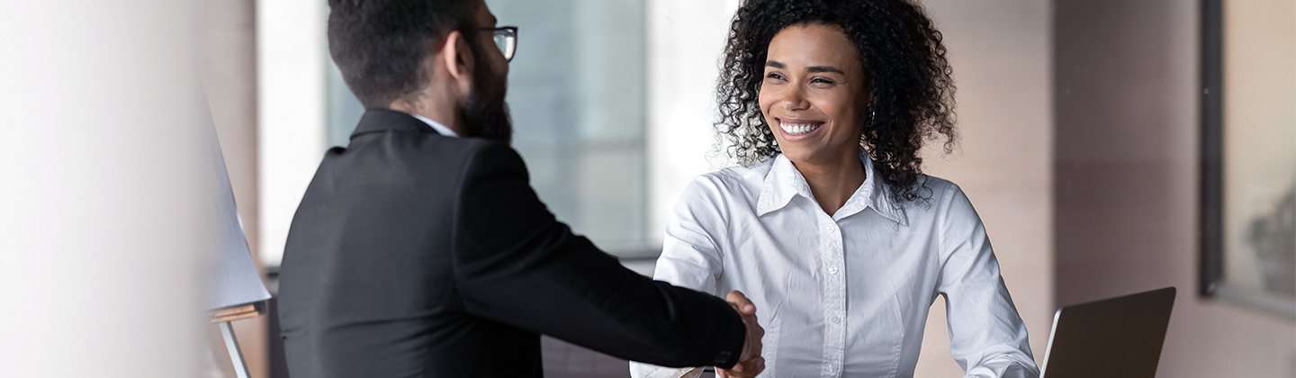 Two business professionals shaking hands at meeting with laptop