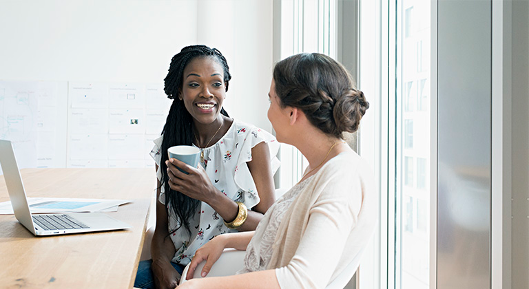 Two people talking in an office setting over coffee