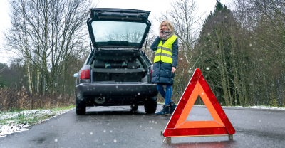 Woman wearing safety vest standing outside of car while on phone