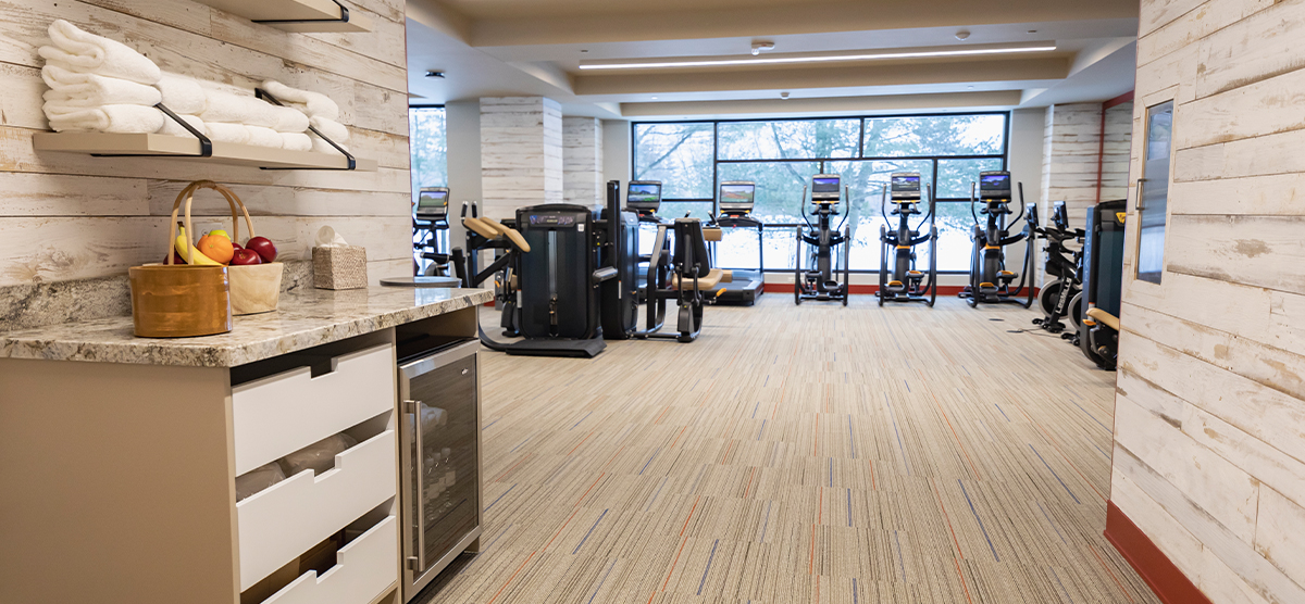 carousel-amenities-fitness-3-1200x556 The Inn fitness center entrance with water and fruit.