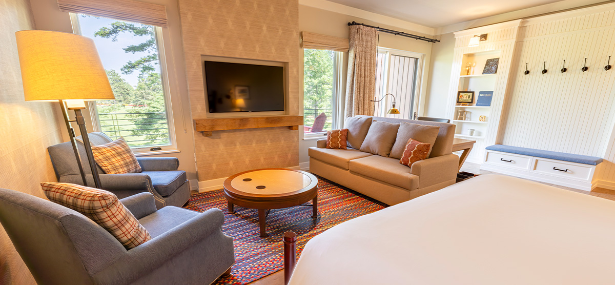 carousel-executive-junior-suite-2-1200x556 King bed with seating area in front of a fireplace.