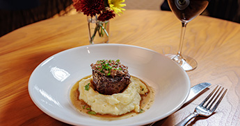 Steak filet with mashed potatoes served on a white plate with a glass of red wine.