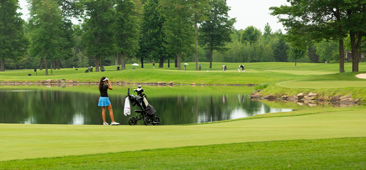 Junior girl standing with her clubs on a green by water. 