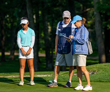 Caddy and rule official talking next to a junior golfer