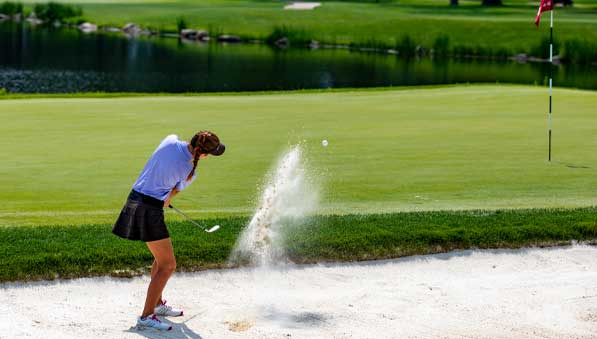 Junior golfer hitting out of a sand trap onto a putting green at SentryWorld