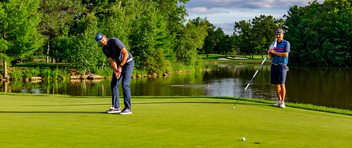 Two people putting on a green next to water at SentryWorld