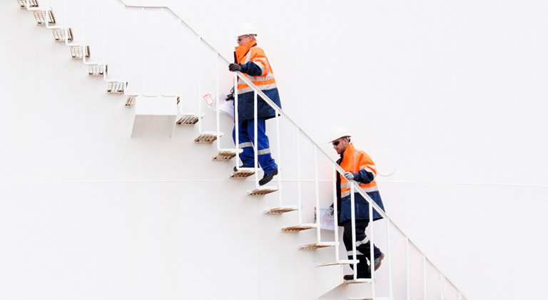 Two workers in hard hats and neon orange climbing along wall.