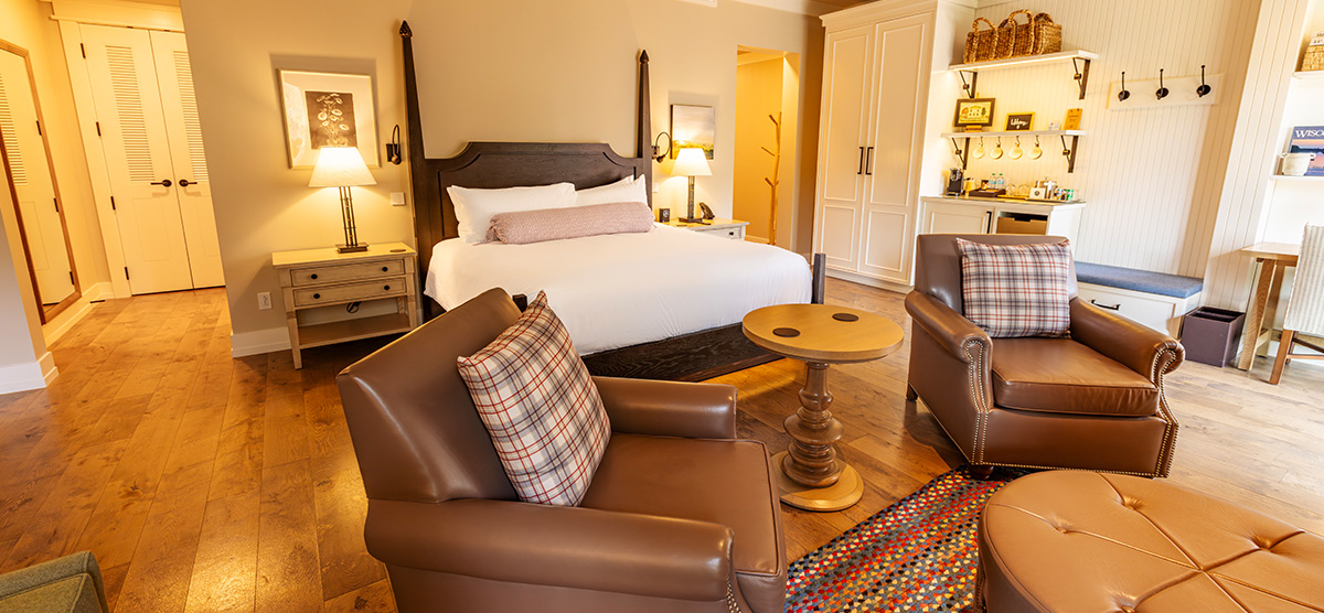 carousel-golf-view-executive-level-luxury-junior-suite-3-1200x556 Suite with king sized bed and seating area with two chairs.