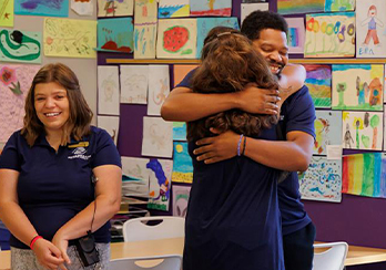 Associates in classroom giving a hug