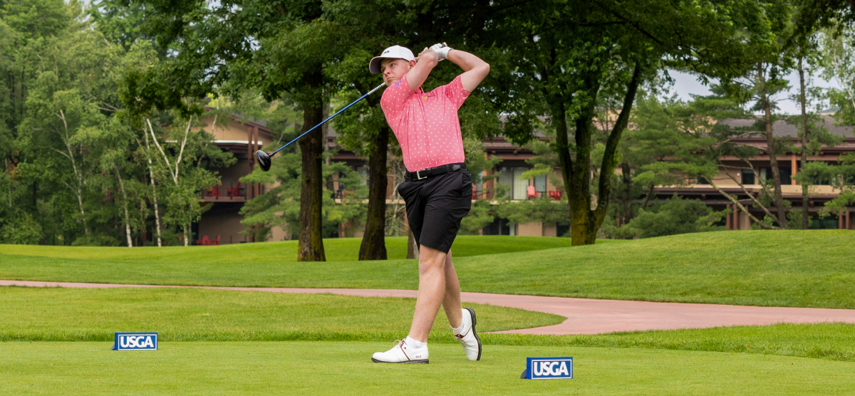 Golfer teeing off with a driver on a golf course.