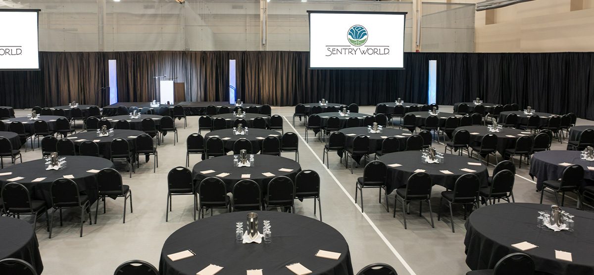 Round tables and a projector screen set for a corporate meeting in the fieldhouse at SentryWorld