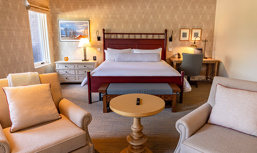 landing-secondary-valentines-inn-840x500 Bedroom with two chairs and a king size bed with a red bed frame.