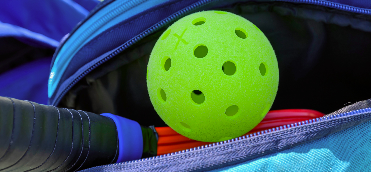 Close-up of a bright green pickleball and a paddle in a blue sports bag.