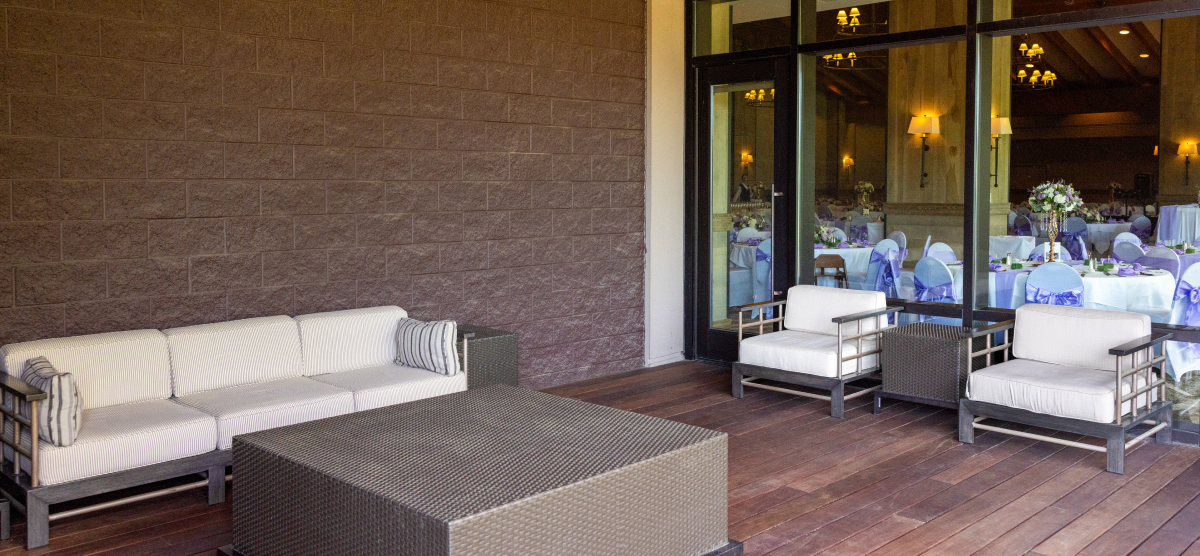 Outdoor patio with sofa and chairs, looking into an event room with decorated tables.