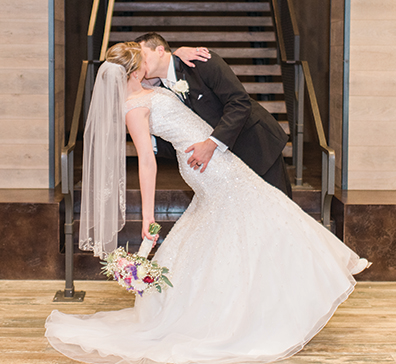 Bride with a flower bouquet kissing a groom in front of stairs at SentryWorld