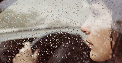 A woman driver looking out car window with raindrops on it