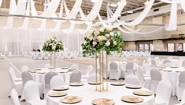 Wedding set up with white tables and chairs in the fieldhouse.