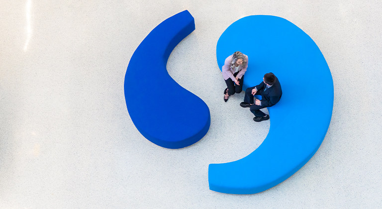 Two people sitting on the Sentry benches that are in the shape of quotation marks