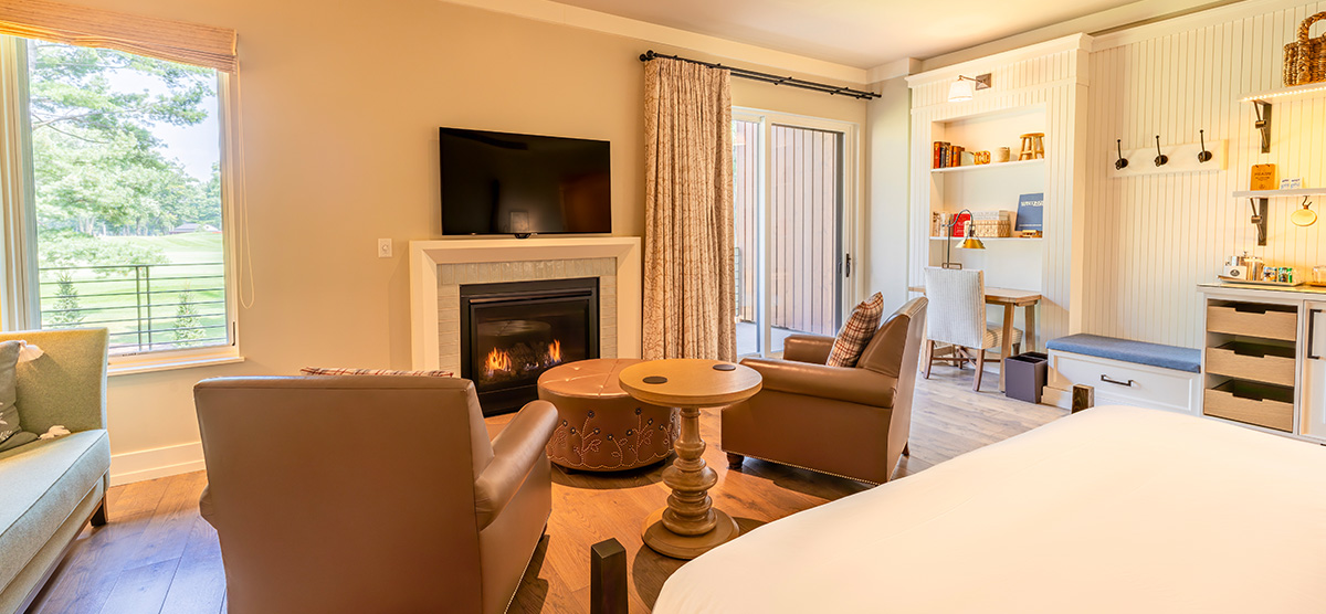 carousel-suite-golf-view-luxury-junior-5-1200x556 King bed and fireplace seating area with two chairs.
