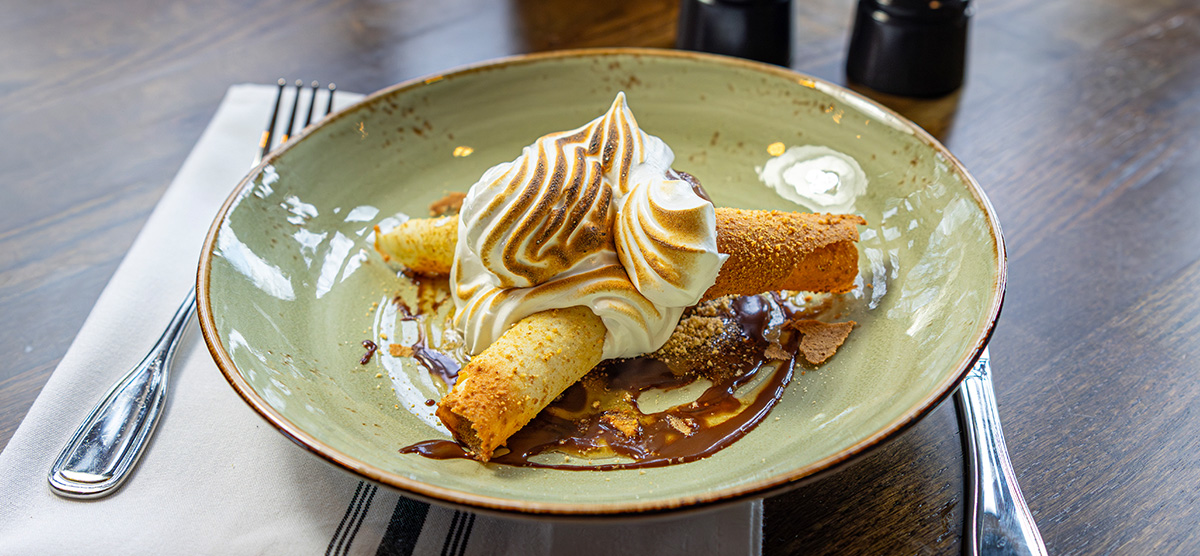 Campfire sundae dessert with dark chocolate ice cream, graham tuille, smoked maple syrup, meringue, and a stout glaze.