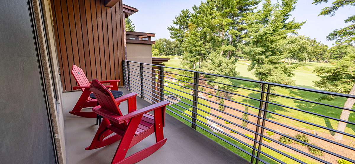 carousel-executive-junior-suite-6-1200x556 Terrace area overlooking the golf course with two red rocking chairs.