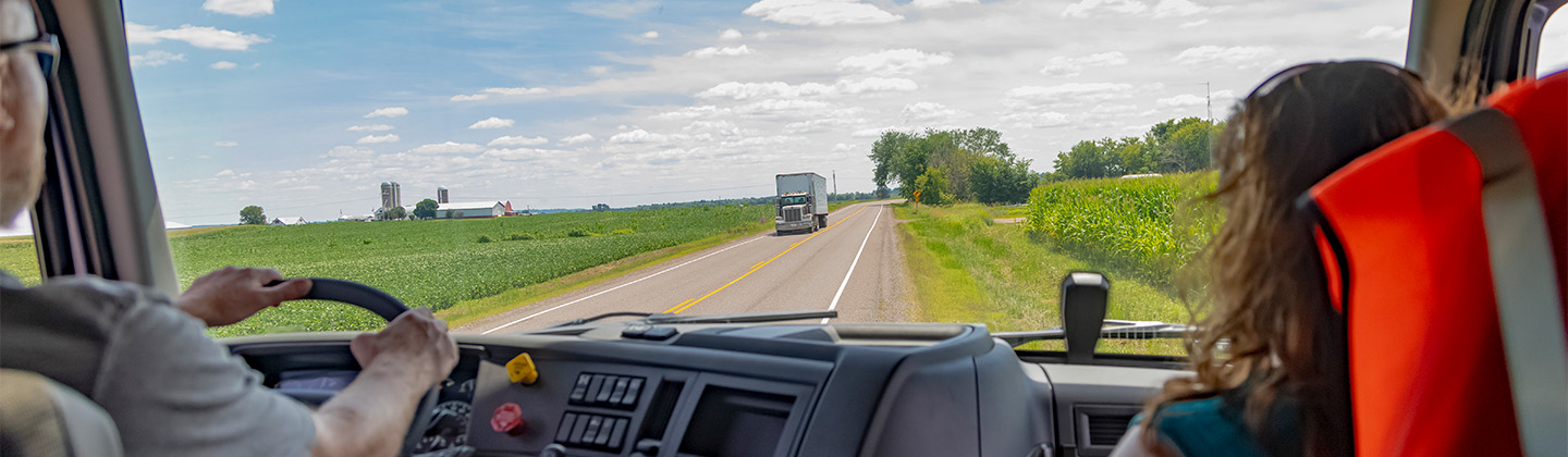 Two people sitting in the semi-truck cab driving on road