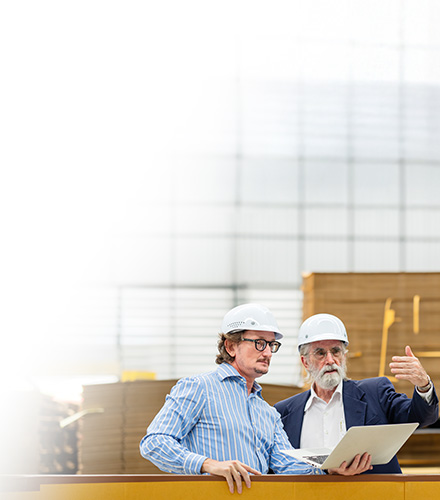 Two men wearing hard hats looking at a laptop in a warehouse
