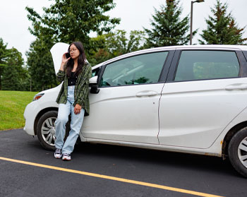 Person leaning on side of a white Toyota Prius with hood up talking on phone