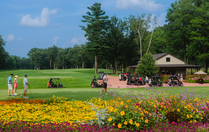 Golf group teeing off on hole one with golf carts and a refreshment station behind.