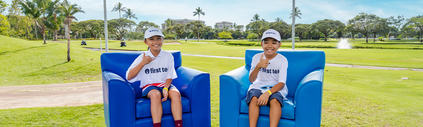 Two happy First Tee kids seated in armchairs on golf course