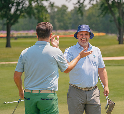 Two men celebrating on the golf course with a high five. 