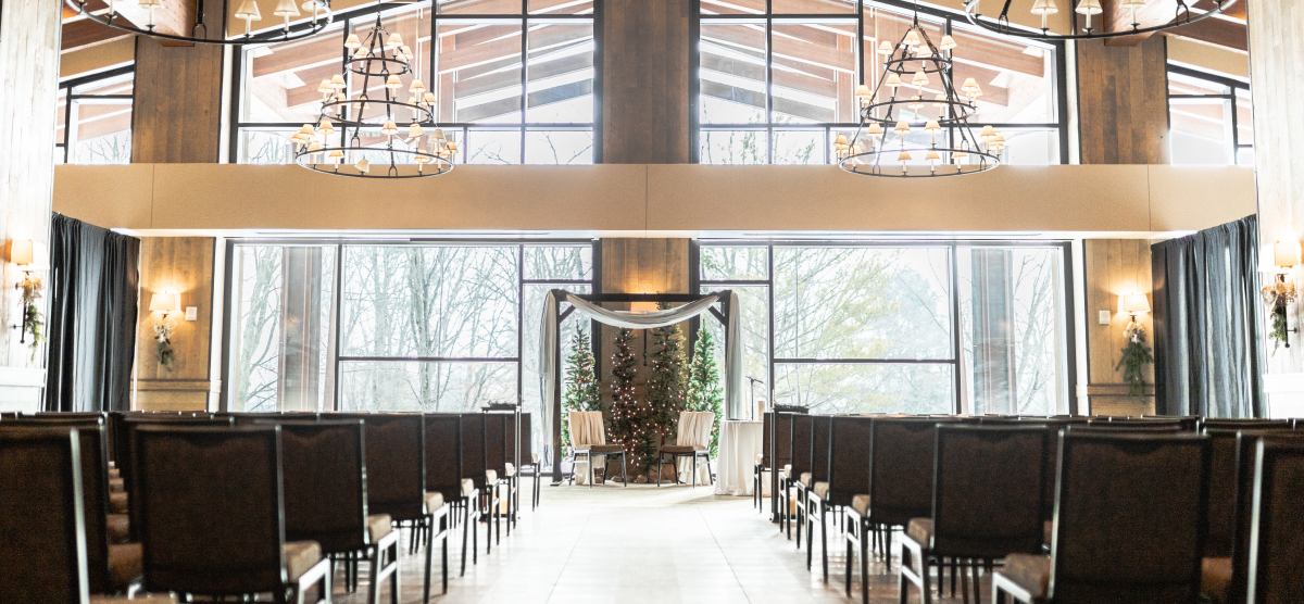 Indoor ceremony with rows of chairs, a chuppah, and decorated trees at the altar.