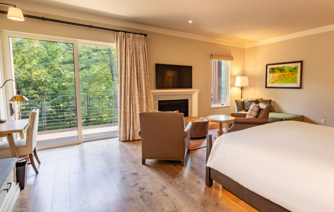 Hotel room with a bed, chairs in front of a fireplace, a desk, and a patio window with balcony.