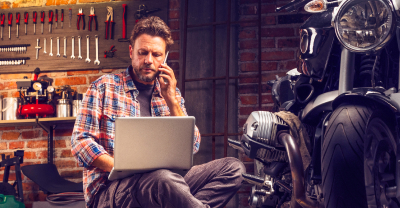 Man on phone and computer next to motorcycle