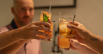 Four friends clinking cocktail glasses while seated at a table in Muse. 