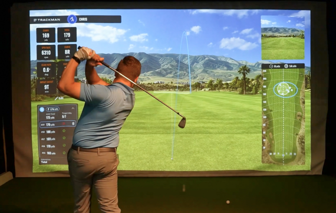 Man swinging a golf club in the SentryWorld golf simulator, with course projected on screen.
