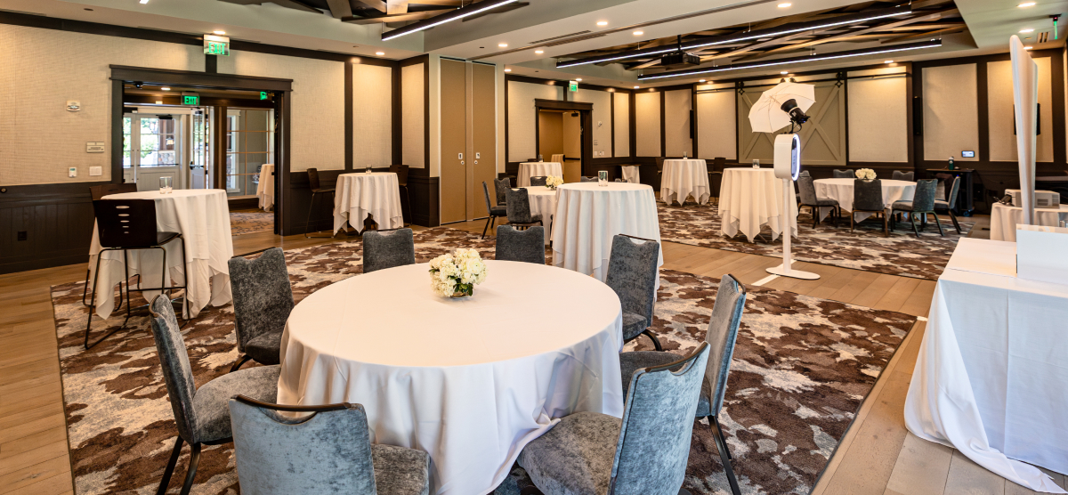 Event room with round tables, high-top tables, chairs, and a photo booth setup.