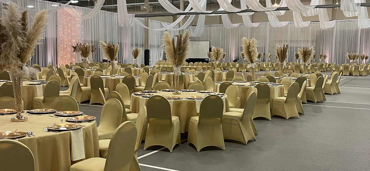 carousel-wedding-venue-fieldhouse-4-1200x556 Many gold covered round tables and chairs set up for a wedding in the fieldhouse.