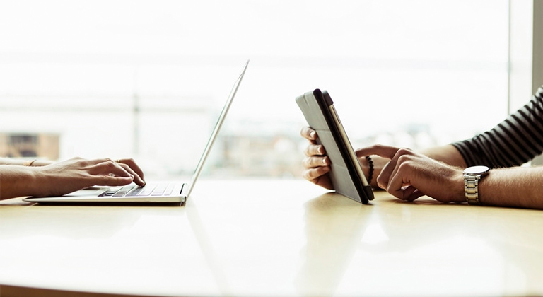 Person typing on laptop another on tablet