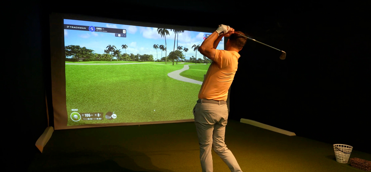 Man in orange shirt swinging a golf club in the SentryWorld golf simulator.