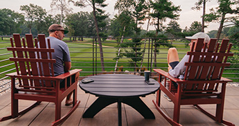 Two men sitting in chairs on a balcony at The Inn at SentryWorld overlooking the 18th green.