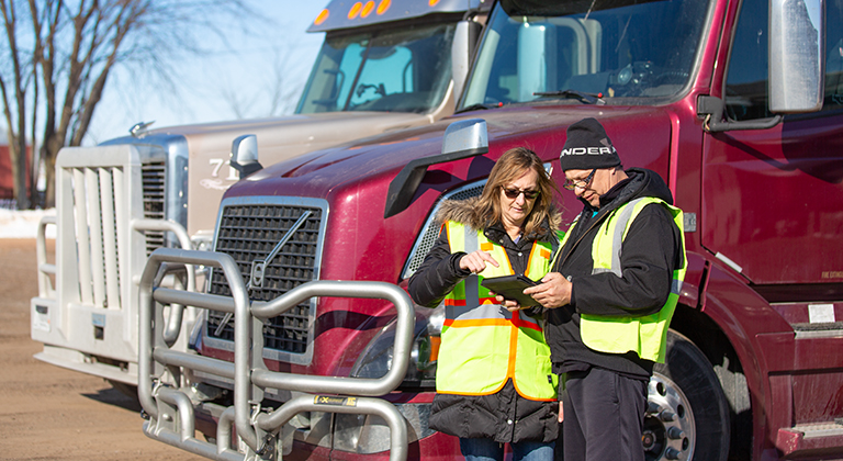 Two drivers look at tablet near their trailer trucks