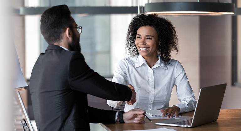 Two business professionals shaking hands at meeting with laptop