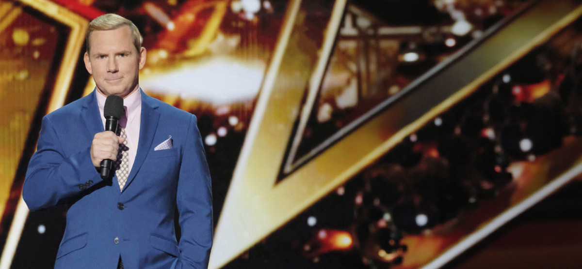 Tom Cotter, a white male, holding a microphone with a gold star background. 